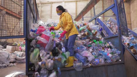 Aufnahmen-Einer-Jungen-Frau-In-Gelber-Jacke-Und-Handschuhen-Schaufeln-Gebrauchte-Flaschen-Mit-Den-Händen-Gebrauchte-Plastikflaschen-In-Einer-Recyclingfabrik