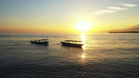 Quiet-paradise-sunset-with-yellow-sky-reflecting-over-tranquil-lagoon-with-silhouette-of-boats-anchored-close-to-shore-of-tropical-island-in-Bali