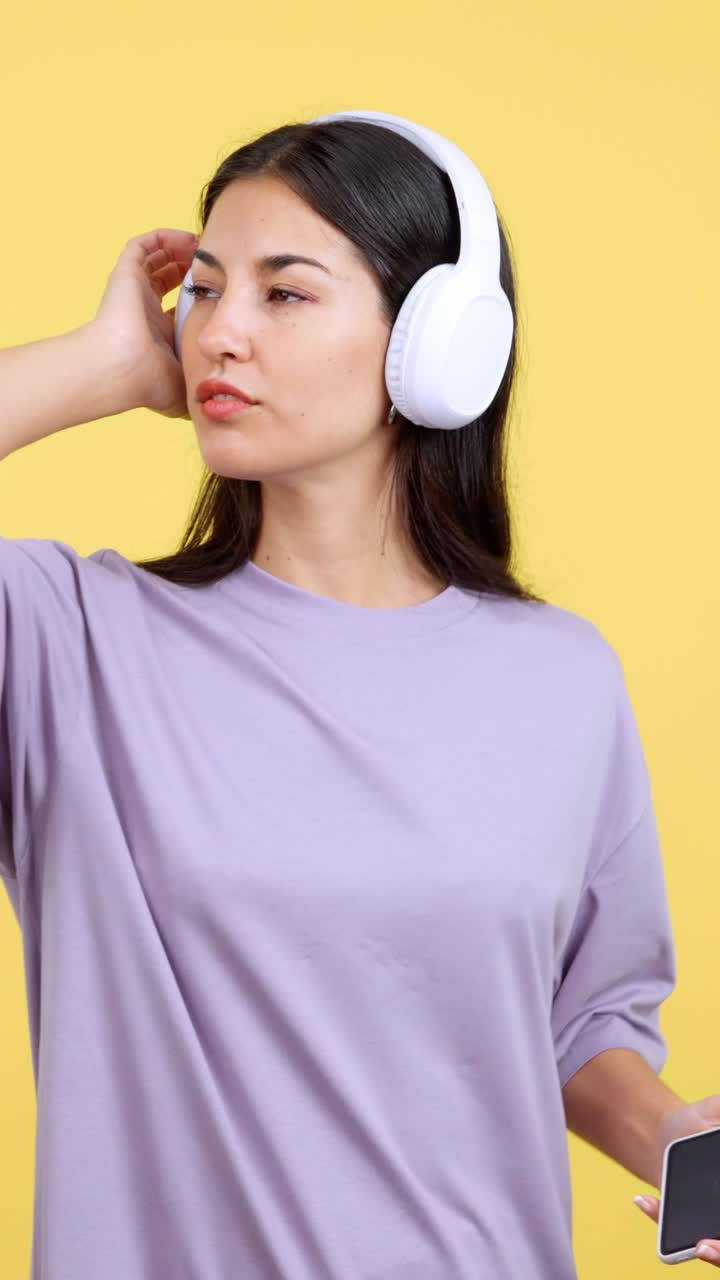 Young woman enjoying music with white headphones on a yellow background