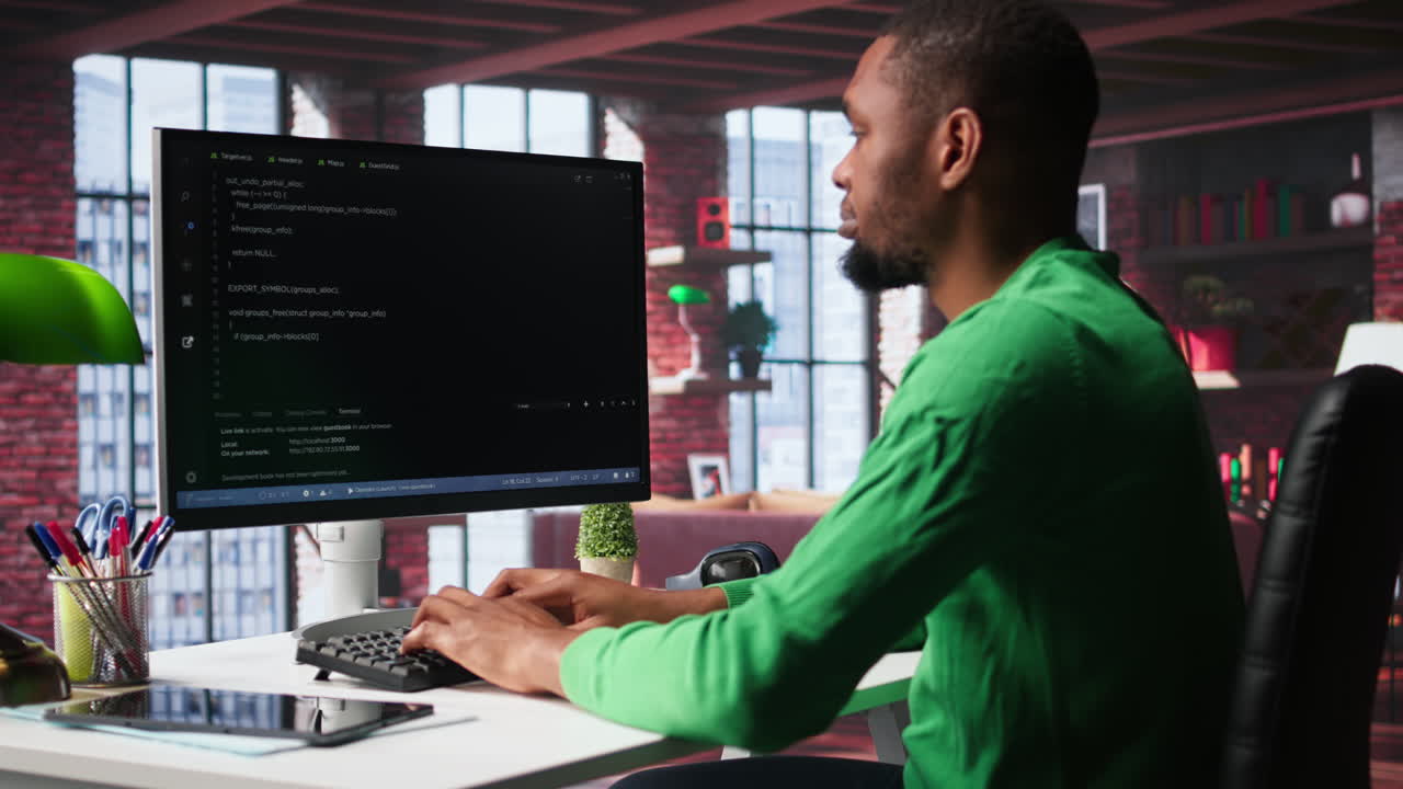 Black technician in home office looks at UI on computer monitor