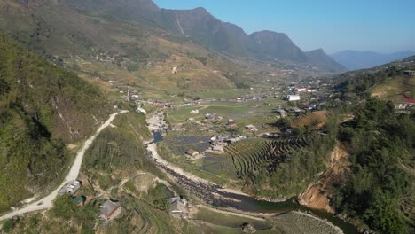 Aerial-drone-shot-of-road-leading-through-villages-amidst-bright-green-rice-terraces-in-the-mountains-of-Sapa,-Vietnam