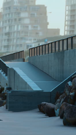 concrete ramp with metal railing leading down to a beach with rocks