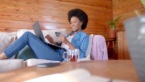 happy african american woman using laptop and credit card in living room, in slow motion