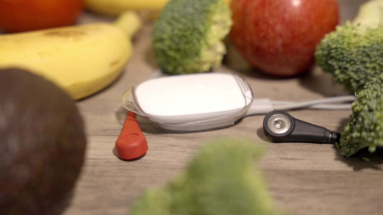 Portable heart monitor rests in warm indoor light among blurred fruit