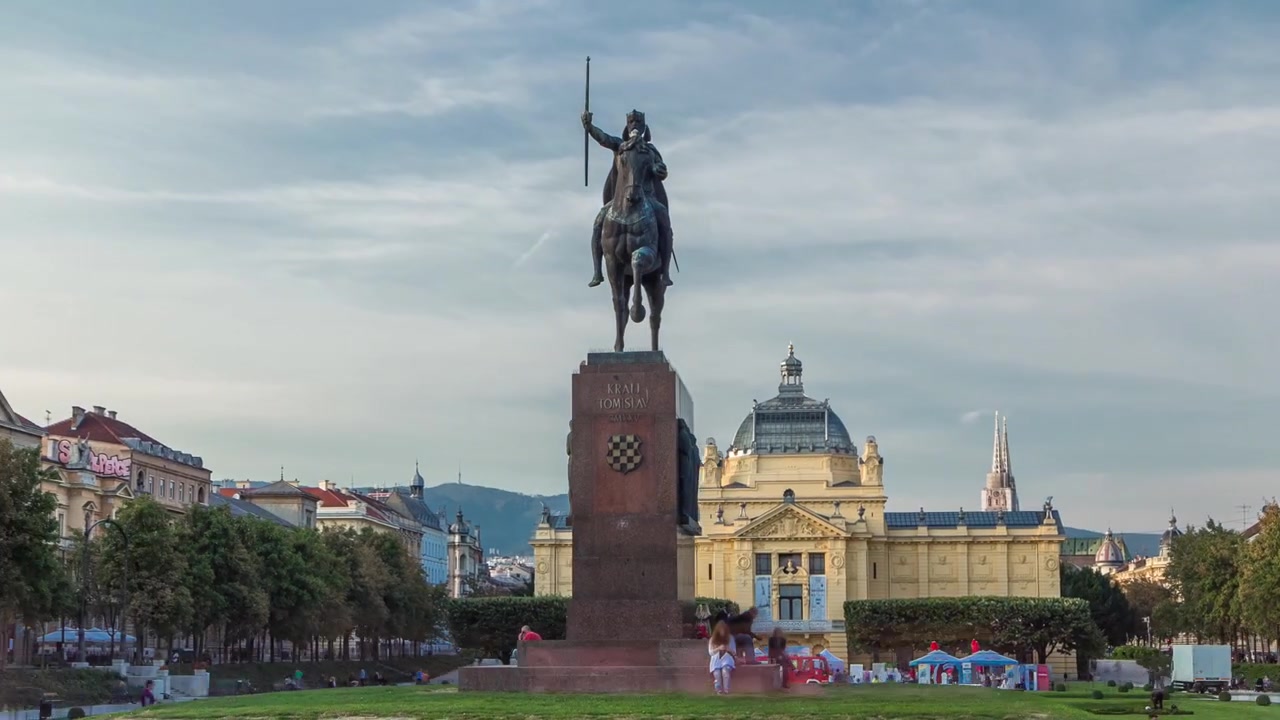 Timelapse hyperlapse do Monumento ao Rei Tomislav da Croácia e pavilhão de arte em parque colorido, em Zagreb, capital da Croácia. Céu azul nublado antes do pôr do sol.