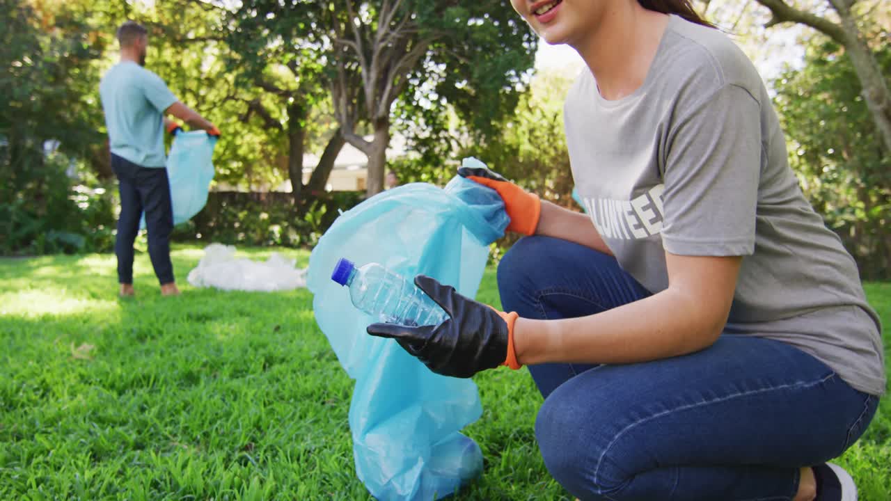 Madre caucasica sorridente che tiene un sacco dei rifiuti, raccogliendo plastica con il marito e il figlio