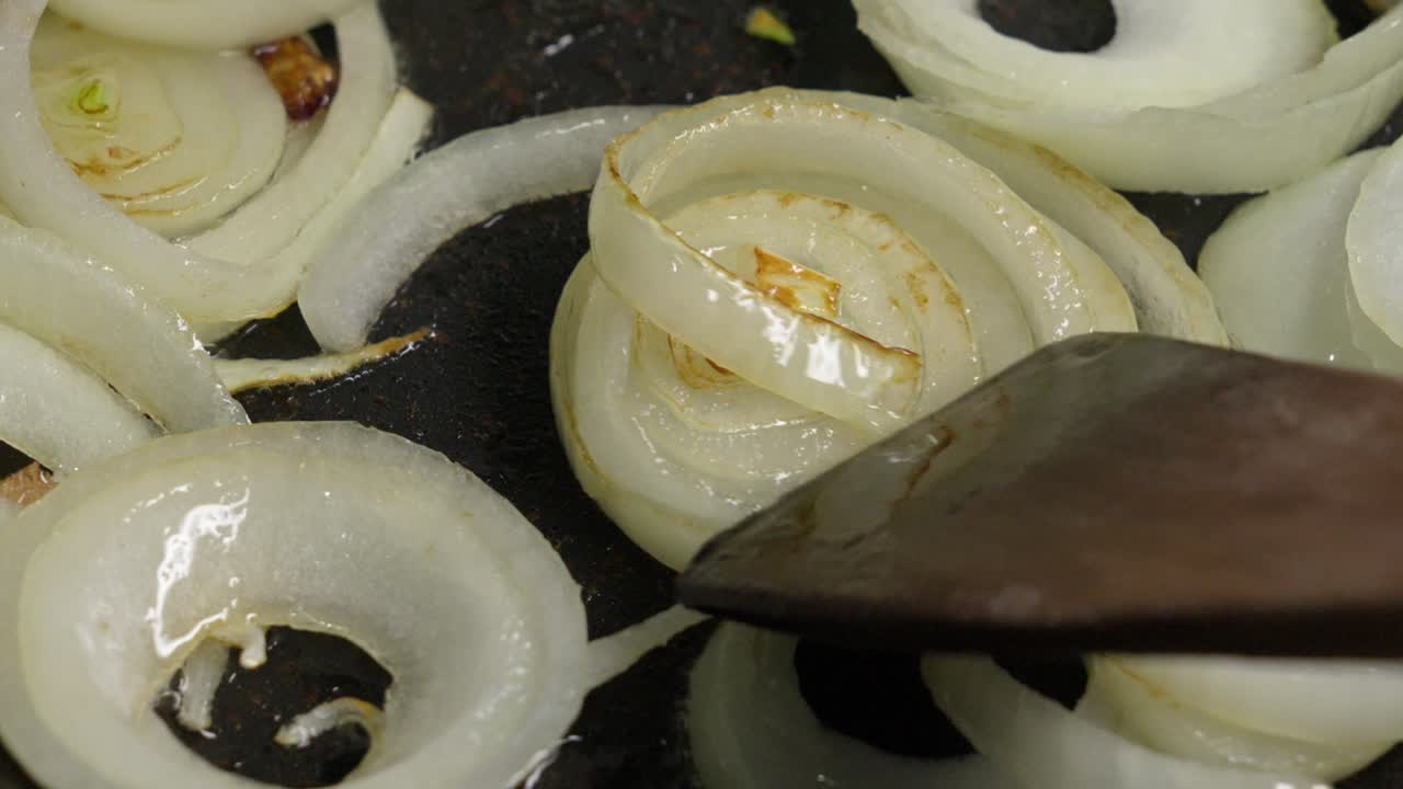 Grilling onion on a pan. Slow motion movement with a wooden spatula