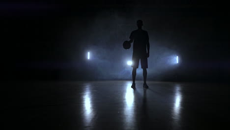 basketball player knocks the ball in the light of the lamps shining behind stands in the duma and knocks the ball on the floor in the basketball hall in slow motion