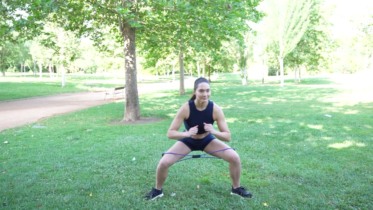 Una donna usa le fasce di resistenza per esercizi all'aperto in un parco, per dare priorità alla salute e al fitness.