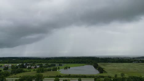 drone footage of storm clouds rolling over green fields and a pond, capturing the dynamic weather patterns and serene landscape