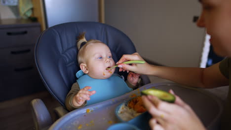 caring caucasian mom giving some avocado to her baby. funny kid grimaces and coughs from the healthy fruit.
