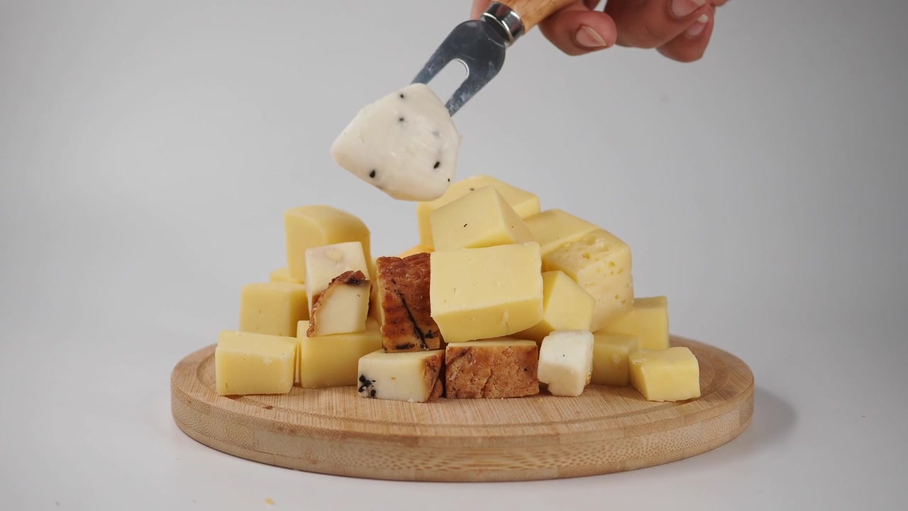 Mano che usa una forchetta per prendere un pezzo di formaggio da un tagliere di legno