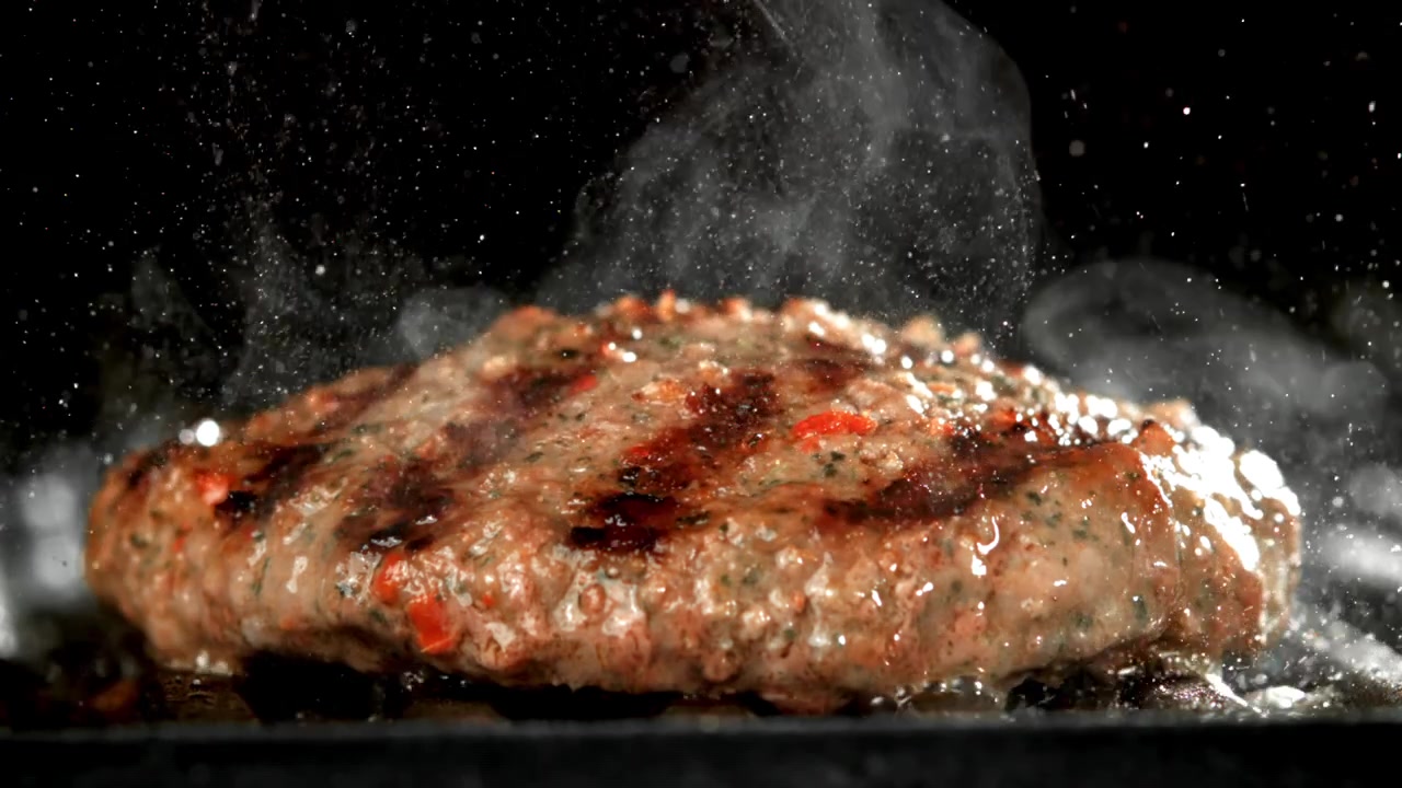 Lækker burgerbøf, der syder på en varm grill i slowmotion