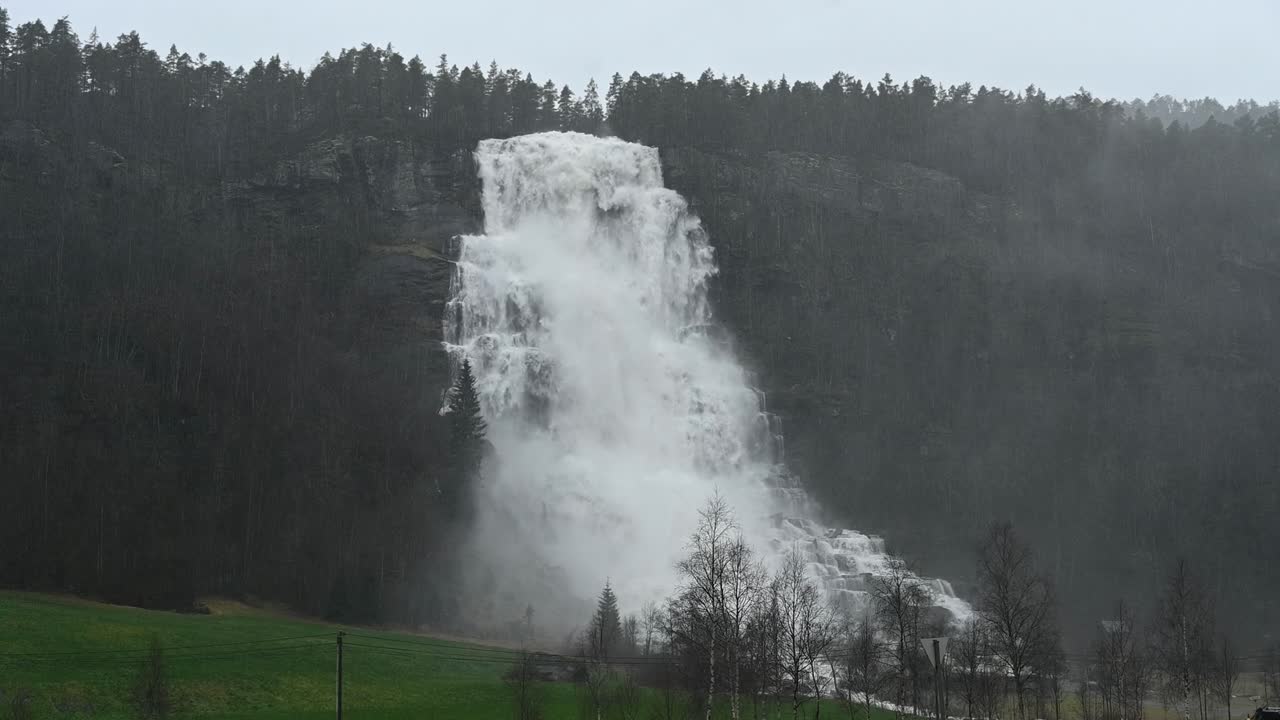 Handheld view of powerful Tvindefossen waterfall surging during rainstorm in Voss, Norway. Flooding and extreme water flow caused by heavy rainfall