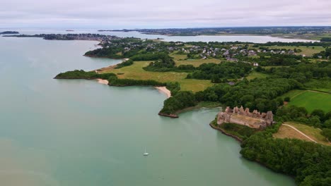 distanced drone view of the beautiful guildo castle aka château du guildo with saint-jacut-de-la-mer commune in the background, arguenon, côtes-d'armor, brittany, france.