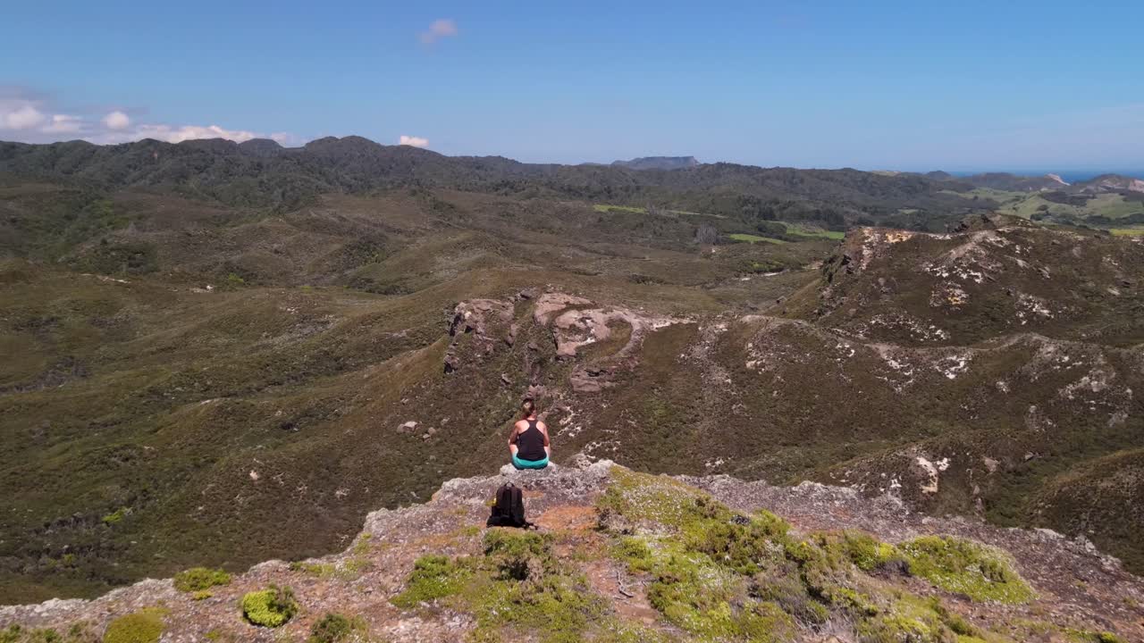 mujer joven sentada en un acantilado y disfrutando de la vista panorámica de cape farewell, nueva zelanda