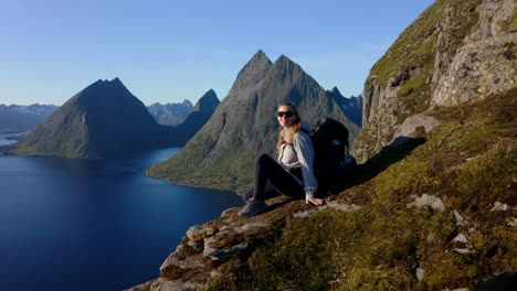 person sits on a cliff overlooking a breathtaking fjord and majestic mountains