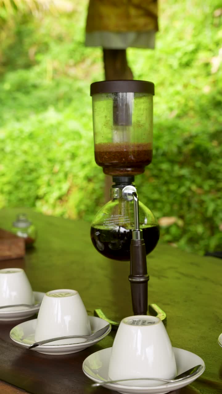 Siphon coffee brews outside with rising steam and warm light on glass chamber detail, vertical handheld static