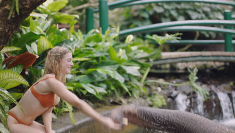 Schöne-Frau-Füttert-Elefanten-Im-Zoo,-Spielt-Im-Pool-Und-Spritzt-Wasser.-Touristin-Hat-Spaß-Bei-Einem-Exotischen-Urlaub-Im-Tropischen-Waldschutzgebiet