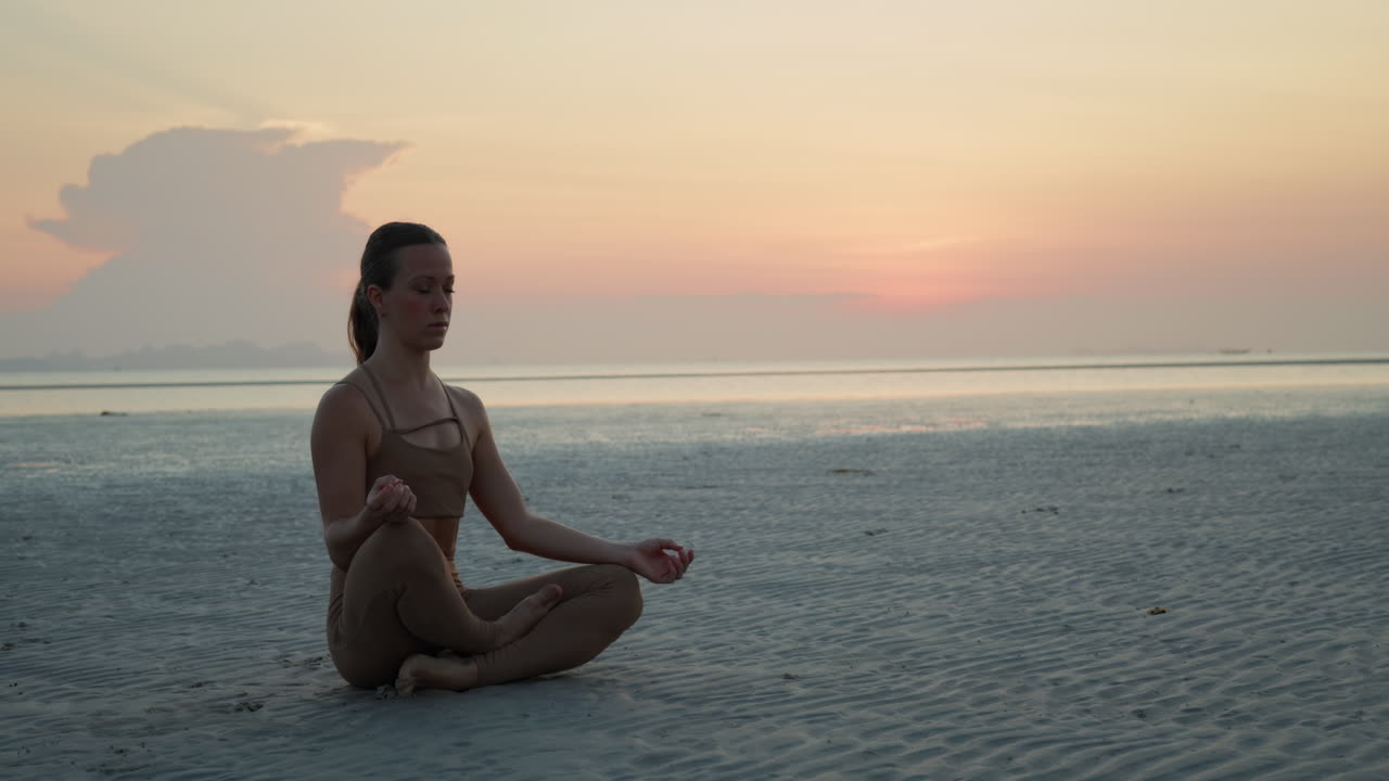 Woman Meditating in Lotus Position on a Serene Beach at Sunset