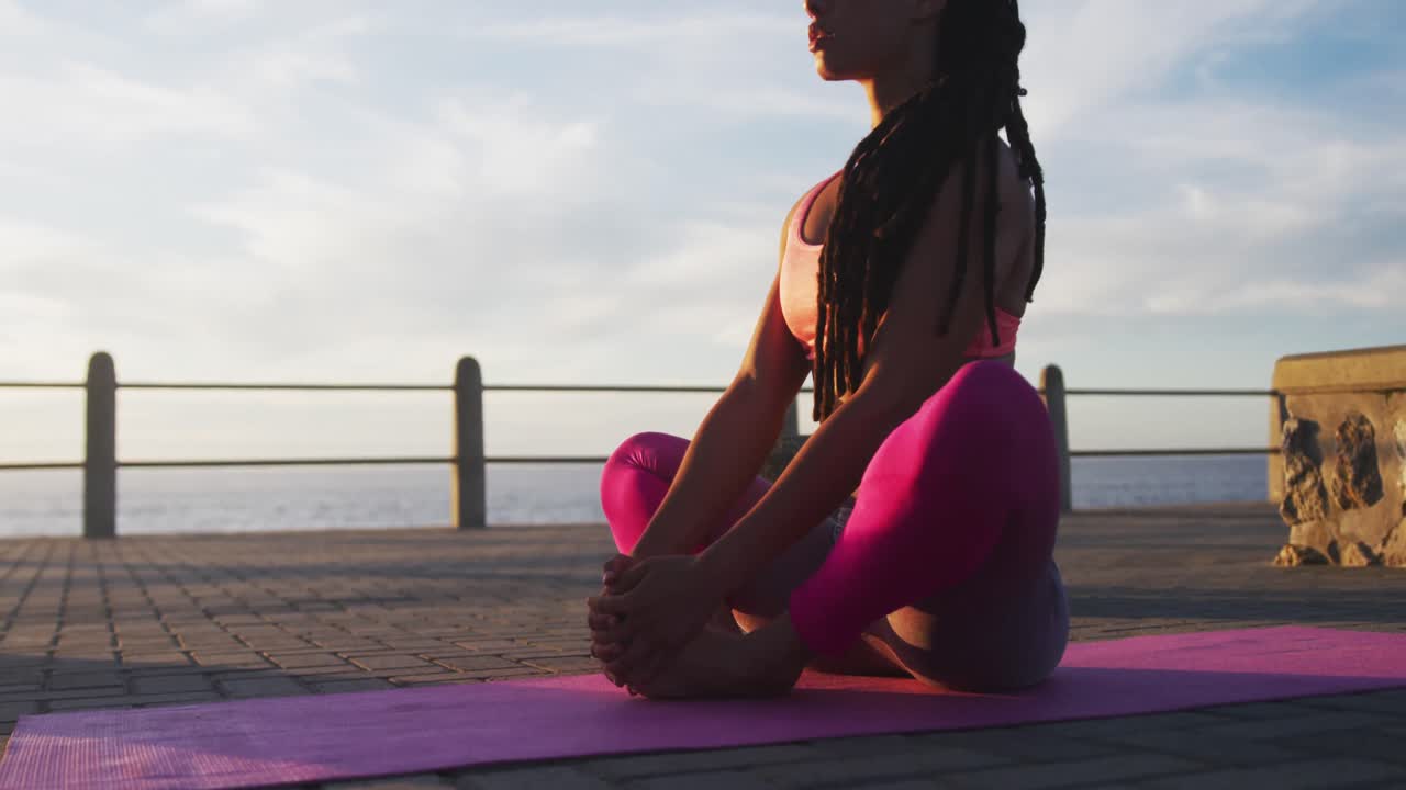 African american woman in sportswear doing yoga on promenade by the sea