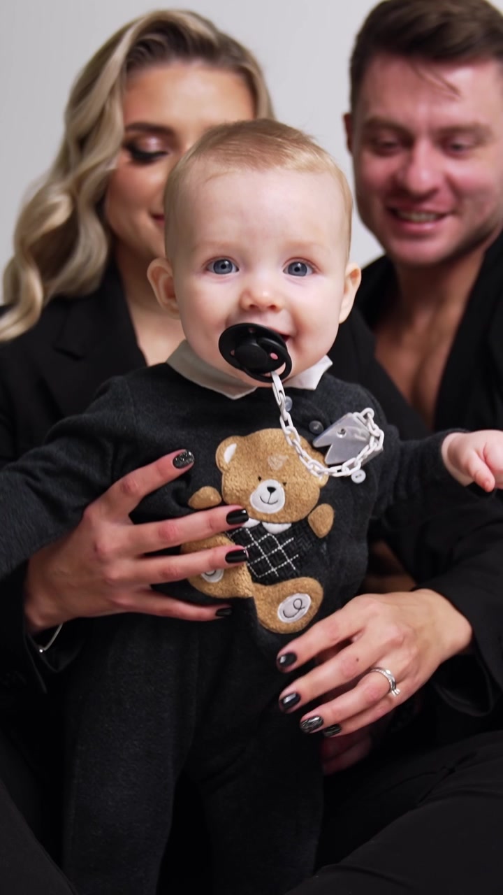 Proud young parents with their lovely infant baby. Cute child with pacifier in mouth tries to stand himself. White backdrop. Vertical video