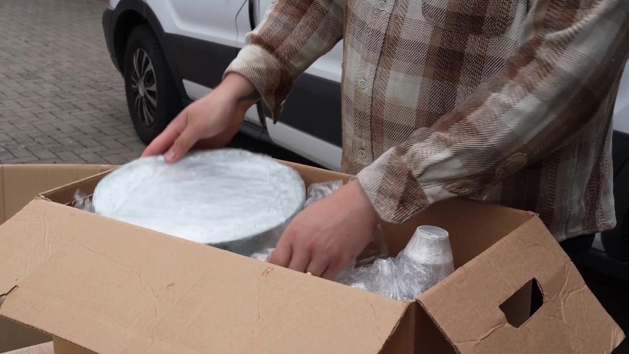 Persona con camicia a quadri imballa prodotti confezionati in una scatola di cartone, riutilizzando vecchio pluriball per un'evasione degli ordini ecologicamente consapevole