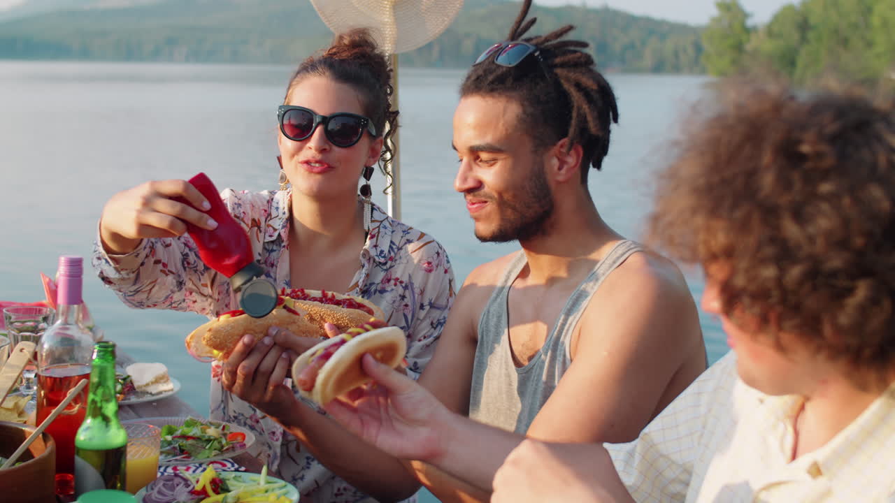 amigos alegres comiendo perritos calientes en la fiesta del lago