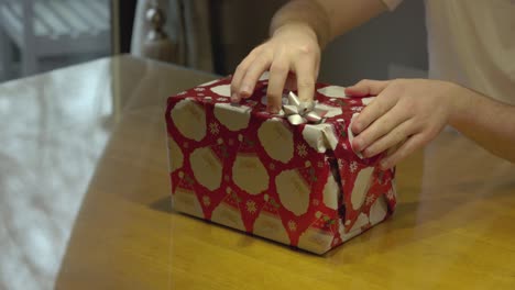 Statische-Aufnahme-Eines-Mannes,-Der-Eine-Schleife-Auf-Ein-Verpacktes-Weihnachtsgeschenk-Klebt