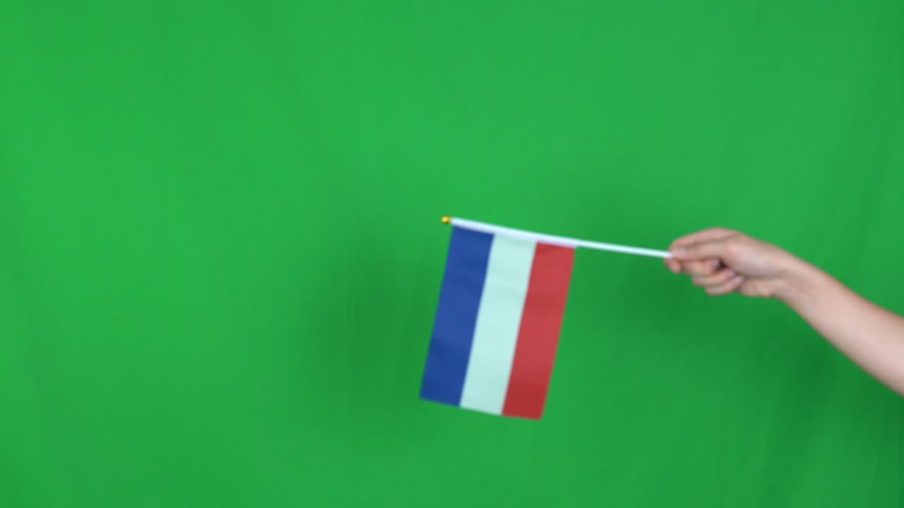 스튜디오에서 녹색 화면 배경에 프랑스 발을 흔들고 있는 알려지지 않은 손의 근접 사진.