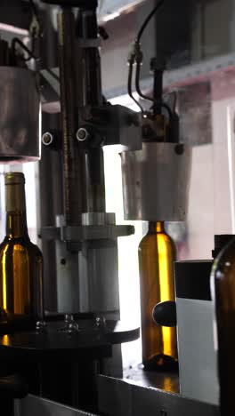 a close-up of an automated bottling machine sealing wine bottles with caps in a production line. the brown glass bottles move through the machine for final packaging in a factory setting.