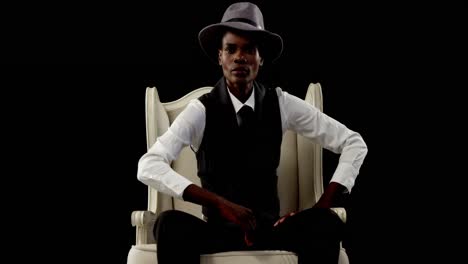 Androgynous-man-posing-on-armchair-against-black-background