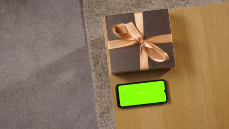 overhead shot man picking up gift wrapped present from table at home with green screen mobile phone