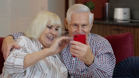 Grandmother-and-grandfather-making-video-call-online-on-mobile-phone-at-home.-Smiling-elderly-couple