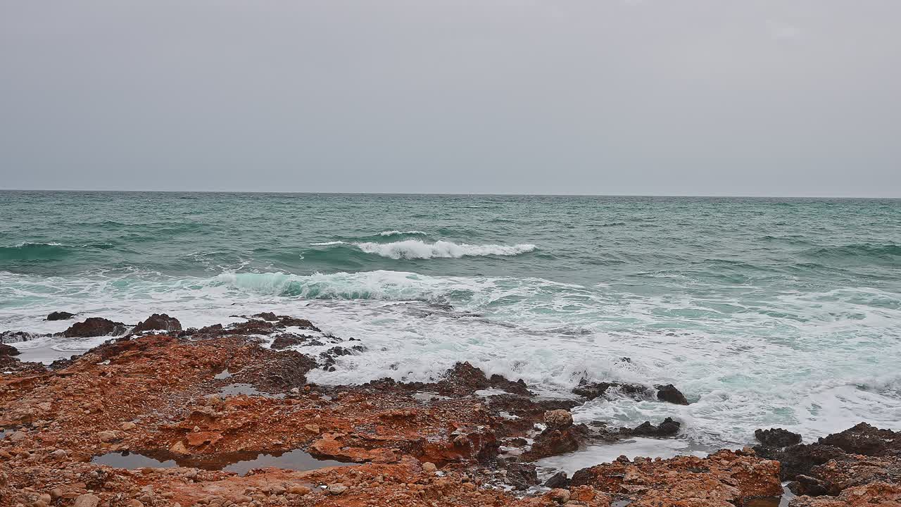खराब मौसम के दिन समुद्र, ग्रे आकाश, नीली लहरें तटरेखा की नारंगी चट्टानों से टकराती हैं