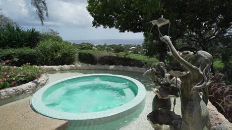 Whirlpool-in-tropical-garden-setting,-bronze-statues-with-fountain-next-to-it,-wide-shot