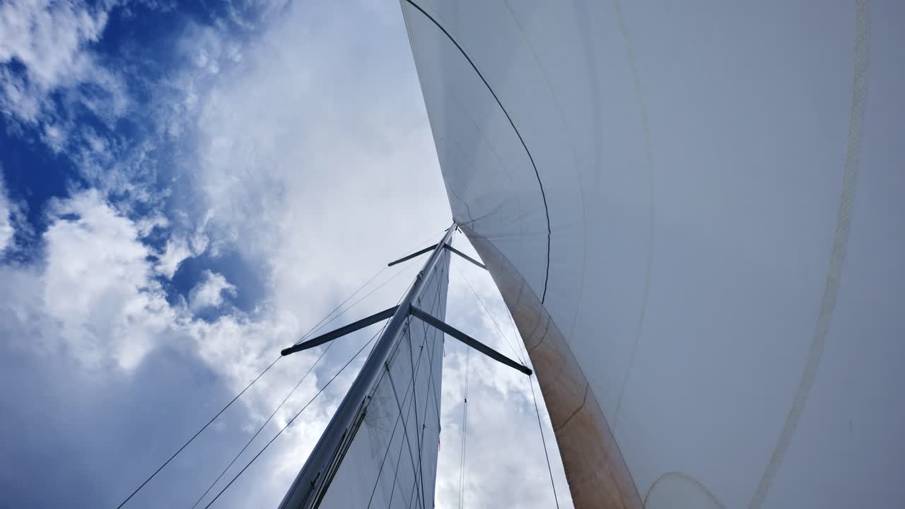 Low angle view of sailboat rig swaying in wind under bright summer clouds
