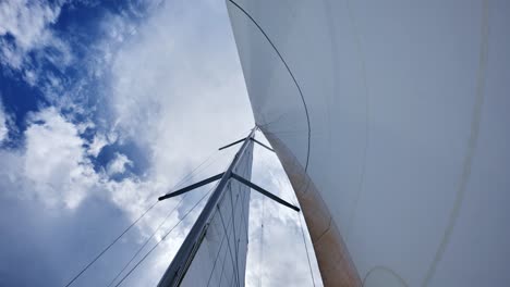 low angle view of sailboat rig swaying in wind under bright summer clouds