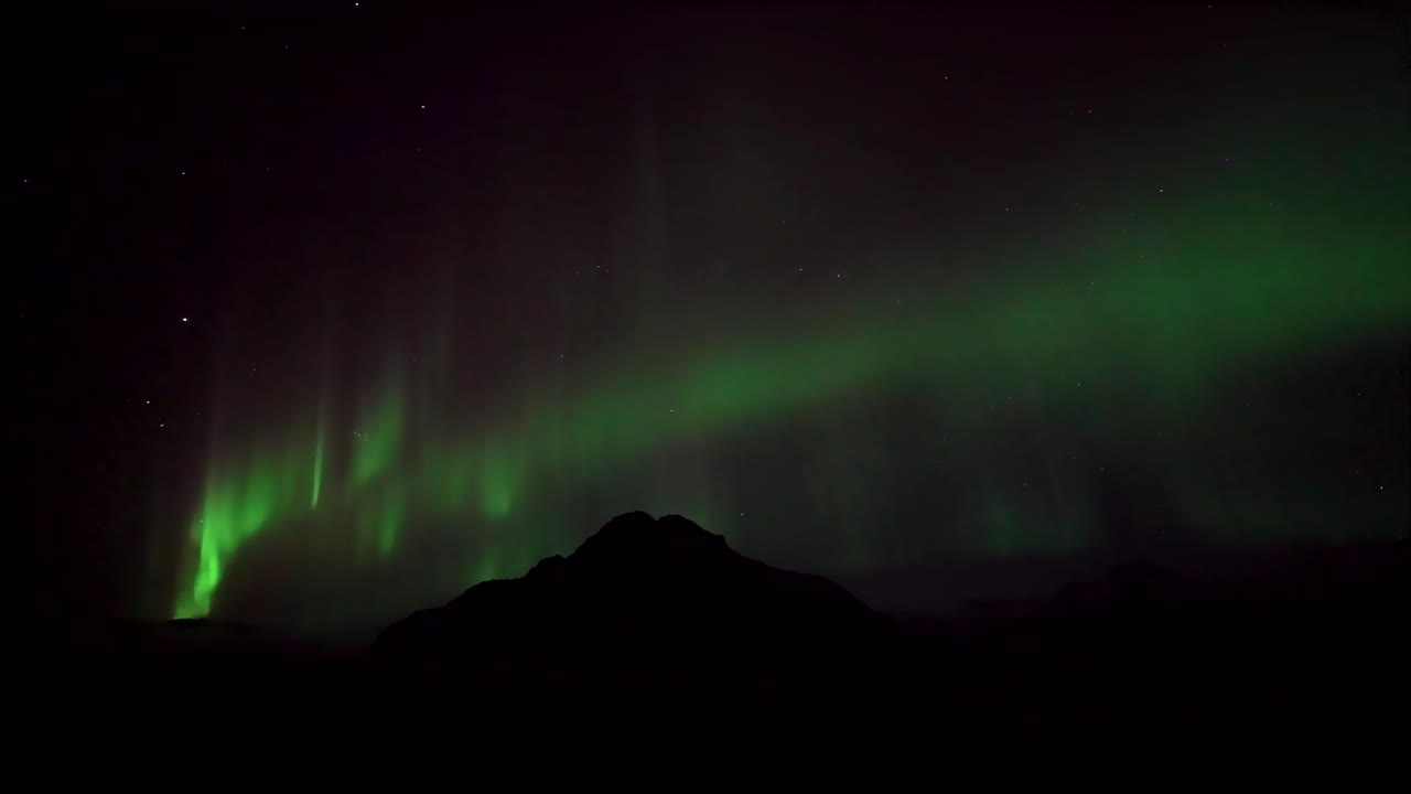 Iceland’s magical Aurora Borealis light up the night sky with vivid green waves, shimmering curtains, and breathtaking solar activity in this stunning Arctic light show over the distant mountains