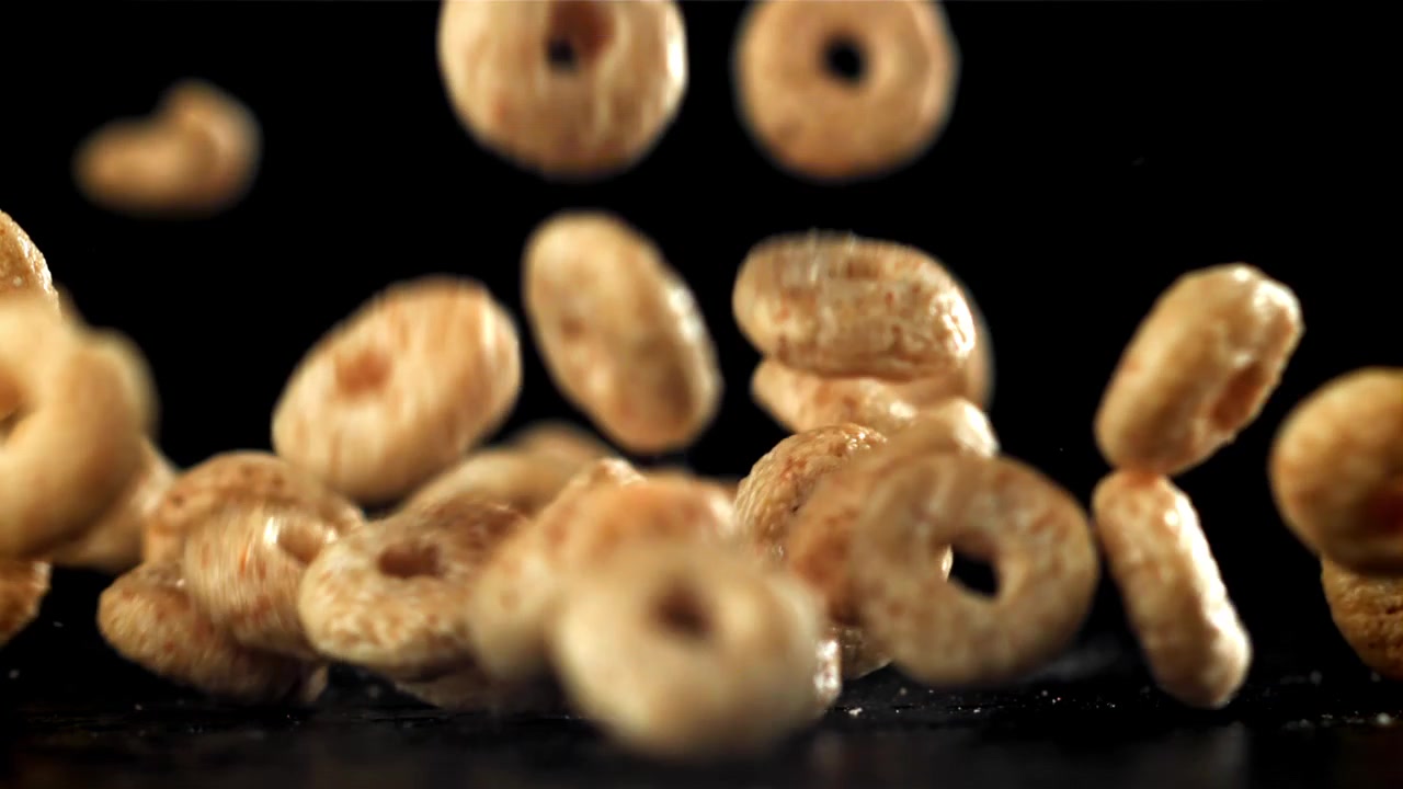Golden Cereal Rings Falling in Slow Motion Against Black Background