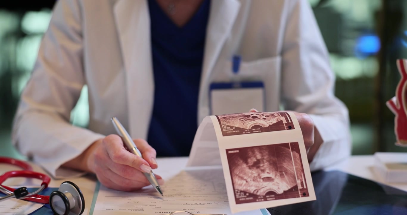 Una dottoressa analizza immagini ecografiche e compila cartelle cliniche.