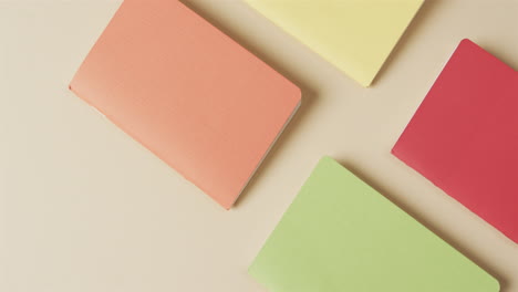 vista aérea de cuadernos de colores dispuestos sobre un fondo beige, en cámara lenta