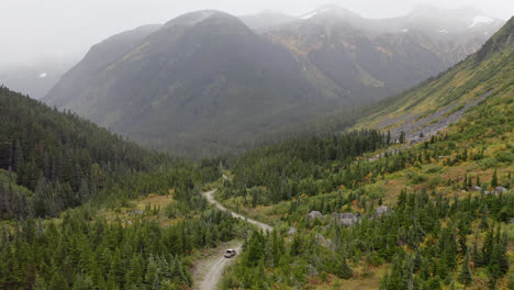 Scenic-valley-with-car-driving-on-dirt-road,-mountains-in-misty-clouds,-aerial