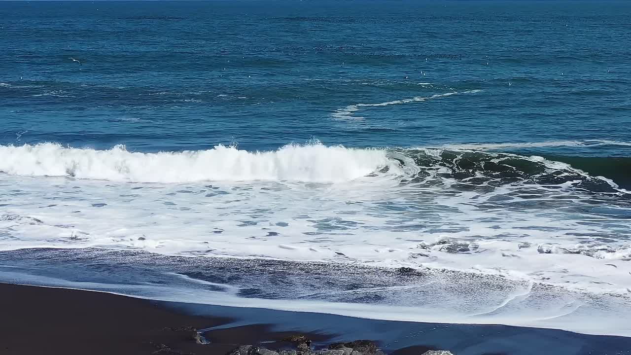 Spiaggia con sabbia nera e onde in Cile di giorno.