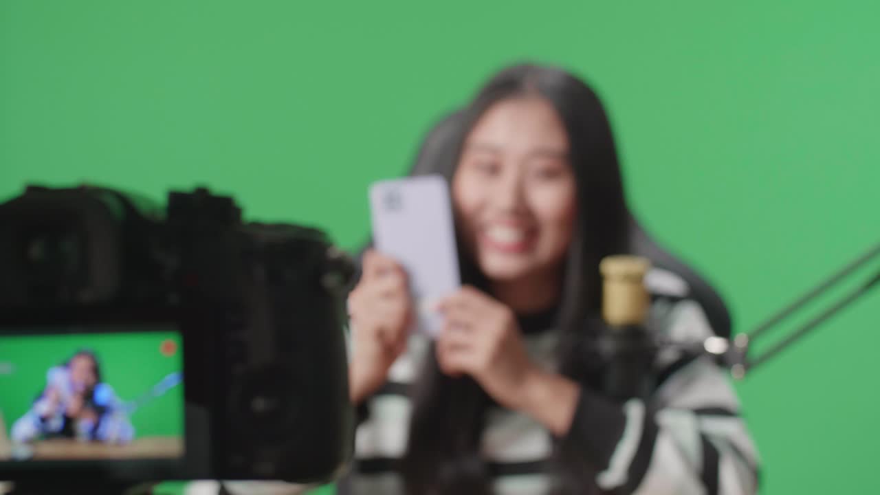Close Up Of A Camera Monitor Recording Asian Woman With Headphone And Computer Reviewing Phone On Green Screen Background