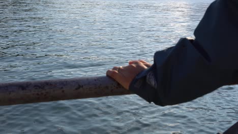 person's hand holds on steel railing by the lake maggiore in laveno-mombello, varese, italy