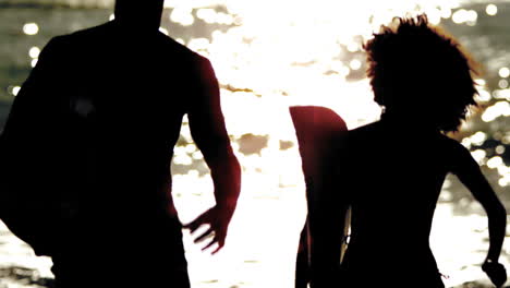 silhouettes of friends holding surfboard and running on the beach