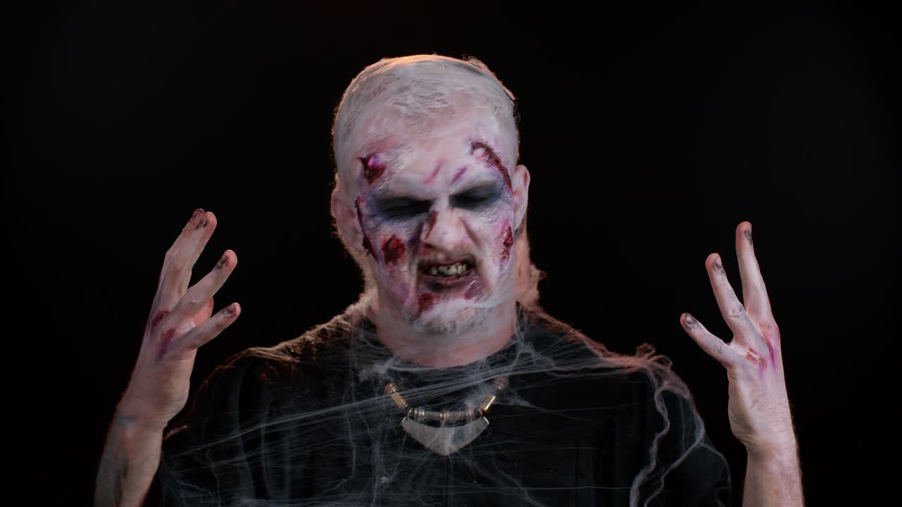 hombre zombi en convulsiones con maquillaje con heridas falsas cicatrices en lentes de contacto blancas tratando de asustar