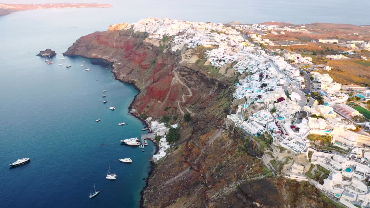 video aéreo del famoso pueblo blanco, colorido y pintoresco de oia construido sobre un acantilado durante la puesta de sol, isla de santorini, cícladas, grecia