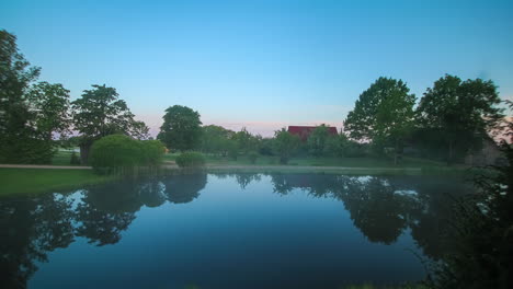 Zeitrafferaufnahme-Eines-Dorfhauses-An-Einem-See-Mit-Aufgehender-Sonne-Im-Hintergrund-Am-Morgen